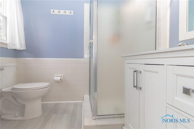 bathroom with a shower with shower door, tile walls, toilet, and vanity