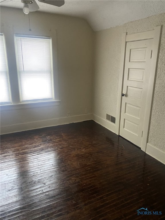 empty room featuring ceiling fan, vaulted ceiling, dark wood-type flooring, and a textured ceiling