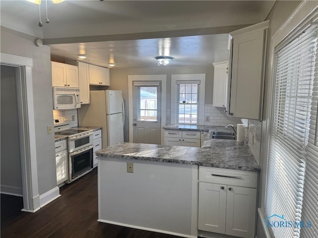 kitchen featuring tasteful backsplash, kitchen peninsula, white appliances, and white cabinetry