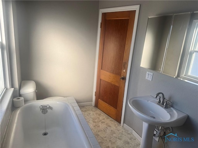 bathroom with a wealth of natural light, toilet, and a bath