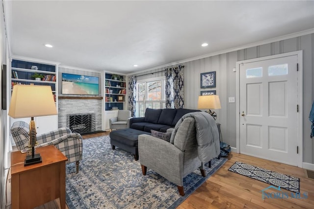 living room featuring crown molding, hardwood / wood-style flooring, a stone fireplace, and built in shelves