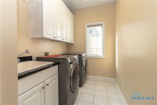 clothes washing area featuring light tile patterned floors, sink, separate washer and dryer, and cabinets