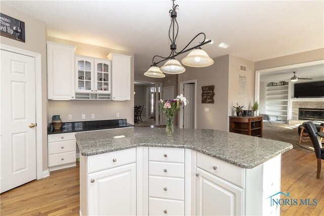 kitchen with white cabinets, a kitchen island, a stone fireplace, hanging light fixtures, and light stone counters