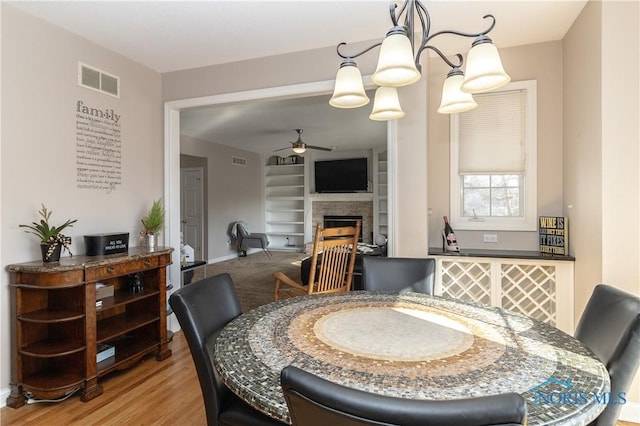 dining area featuring wood-type flooring, built in features, and ceiling fan with notable chandelier