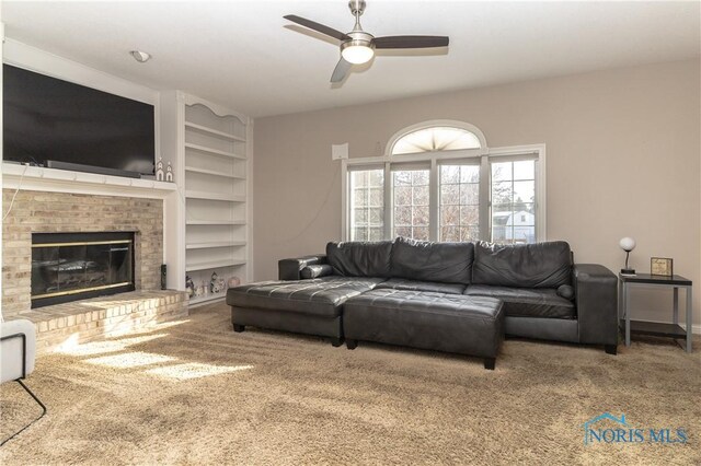 carpeted living room with a brick fireplace, built in features, and ceiling fan