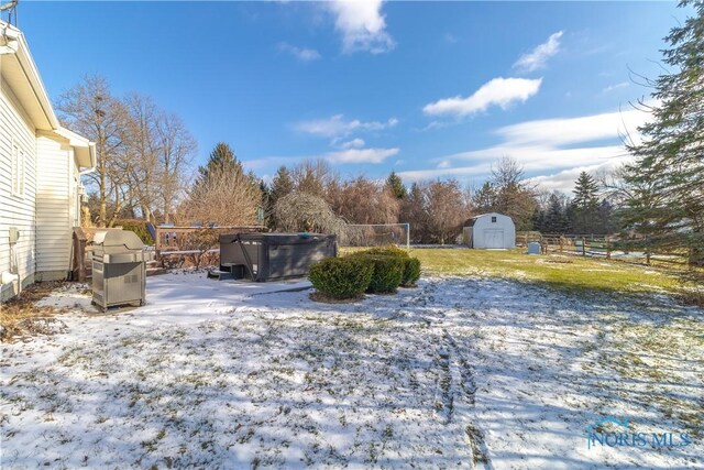 yard layered in snow with a shed and a hot tub