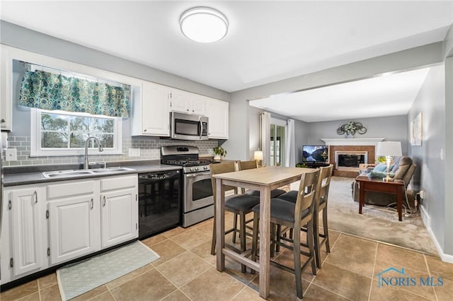 kitchen with a fireplace, tasteful backsplash, white cabinetry, sink, and stainless steel appliances