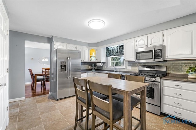 kitchen with light tile patterned flooring, sink, appliances with stainless steel finishes, white cabinets, and backsplash