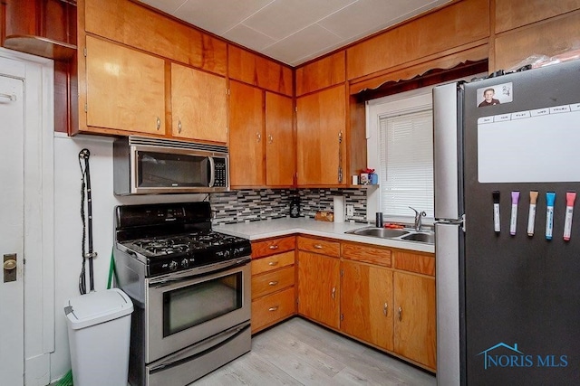 kitchen with light wood-type flooring, backsplash, appliances with stainless steel finishes, and sink