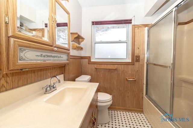 full bathroom with toilet, bath / shower combo with glass door, vanity, and wooden walls