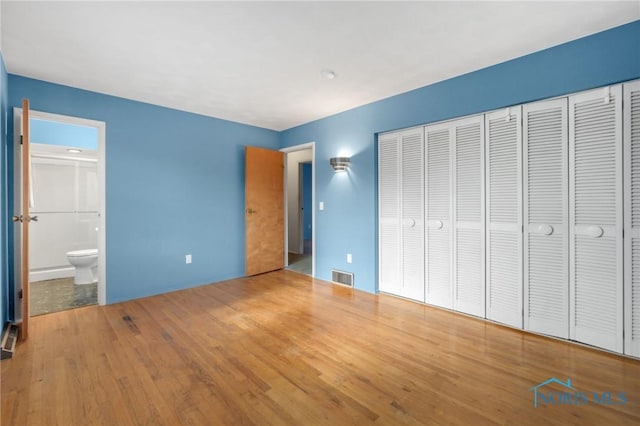 unfurnished bedroom with hardwood / wood-style flooring, ensuite bathroom, and a closet