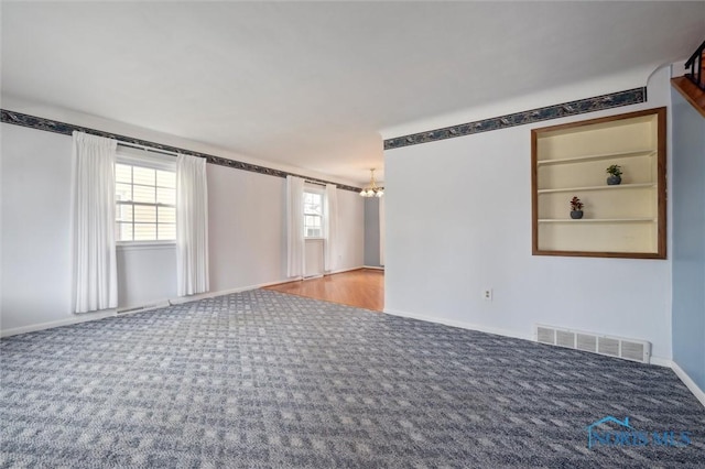 carpeted spare room featuring an inviting chandelier and built in features