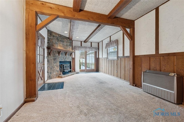 unfurnished living room featuring heating unit, wooden walls, beamed ceiling, a fireplace, and carpet