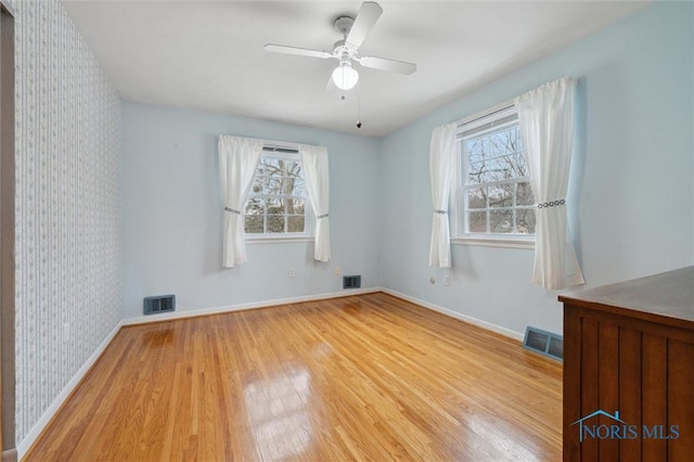 empty room with a healthy amount of sunlight, hardwood / wood-style floors, and ceiling fan