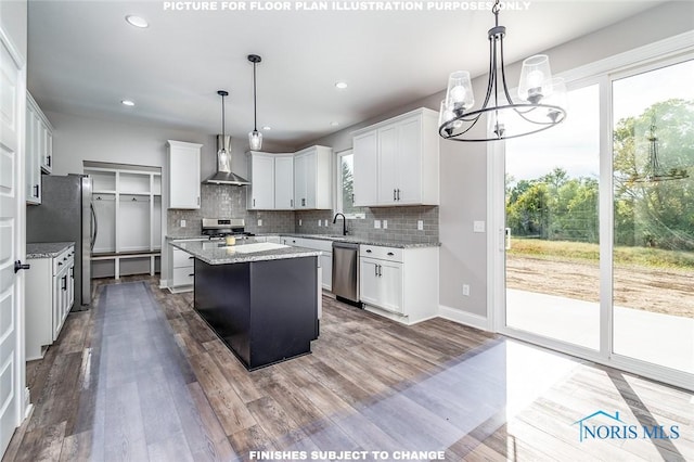 kitchen featuring stainless steel appliances, hanging light fixtures, wall chimney exhaust hood, white cabinets, and a center island