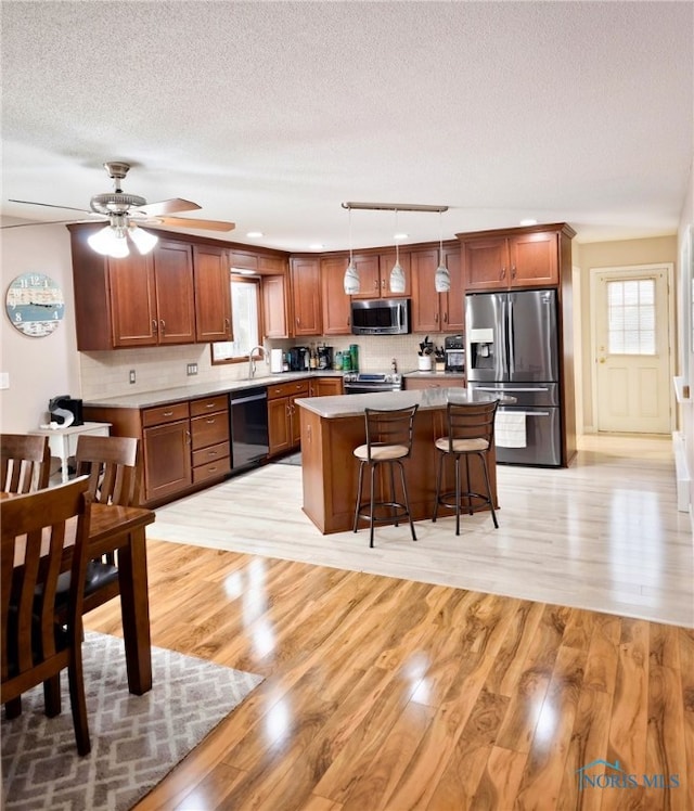 kitchen featuring decorative light fixtures, a kitchen island, appliances with stainless steel finishes, a kitchen breakfast bar, and a textured ceiling