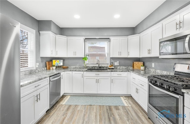 kitchen with white cabinetry, stainless steel appliances, sink, light stone counters, and light hardwood / wood-style flooring