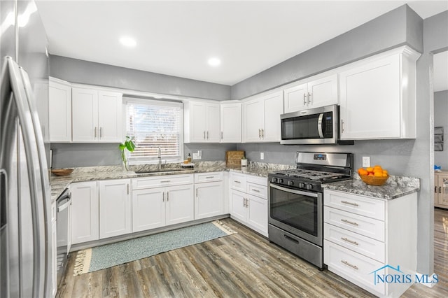 kitchen with appliances with stainless steel finishes, dark wood-type flooring, white cabinetry, sink, and light stone counters