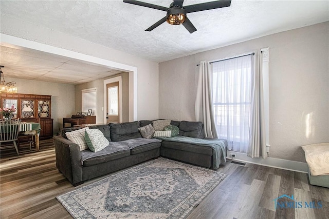 living room featuring ceiling fan with notable chandelier, plenty of natural light, a textured ceiling, and dark hardwood / wood-style flooring