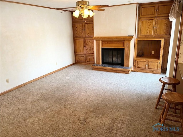 unfurnished living room with ceiling fan, a tiled fireplace, ornamental molding, and carpet flooring