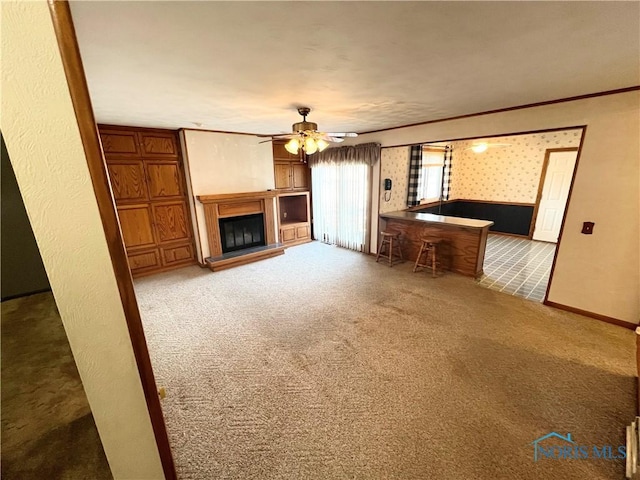 unfurnished living room with ceiling fan, crown molding, and carpet floors