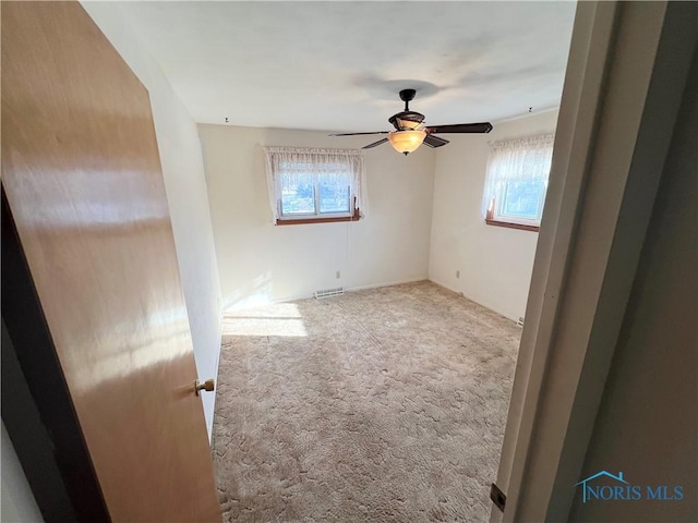 unfurnished room featuring light carpet, ceiling fan, and a wealth of natural light