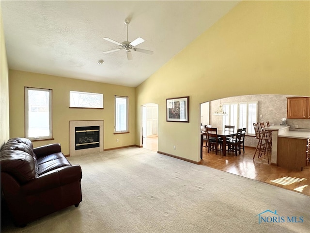 living room with ceiling fan, light colored carpet, a fireplace, and high vaulted ceiling