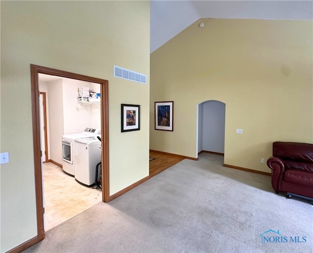 interior space featuring high vaulted ceiling, washer and clothes dryer, and light colored carpet