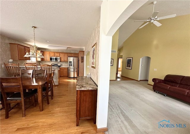 dining room with a textured ceiling, high vaulted ceiling, light hardwood / wood-style floors, and ceiling fan