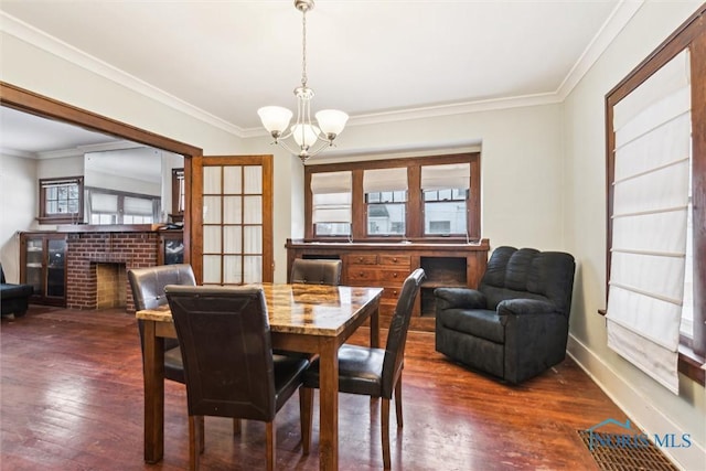 dining room featuring an inviting chandelier, dark hardwood / wood-style flooring, crown molding, and a fireplace