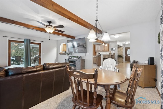 carpeted dining space with ceiling fan and beamed ceiling