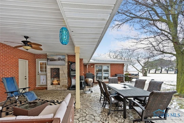 snow covered patio featuring ceiling fan and an outdoor living space with a fireplace