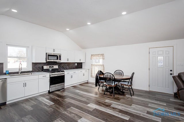 kitchen featuring lofted ceiling, sink, appliances with stainless steel finishes, white cabinetry, and decorative backsplash