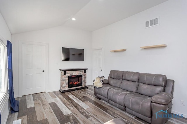 living room featuring a stone fireplace, vaulted ceiling, and wood-type flooring