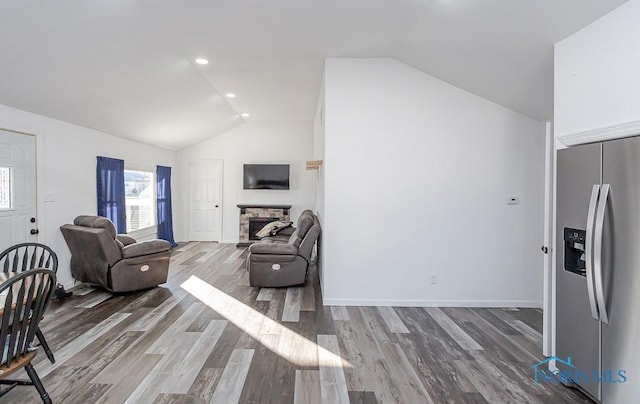 living room with lofted ceiling, a stone fireplace, and hardwood / wood-style flooring