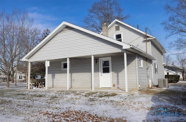 snow covered rear of property featuring central AC and covered porch