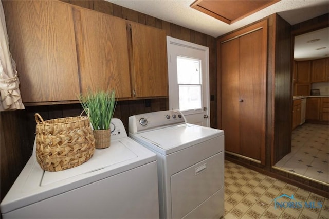 clothes washing area with washing machine and dryer, cabinets, and wood walls