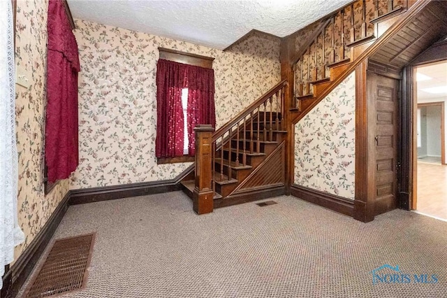 staircase featuring a textured ceiling and carpet flooring