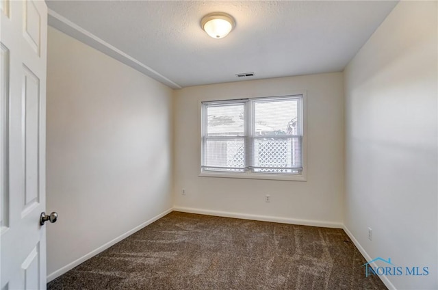 unfurnished room featuring a textured ceiling and dark carpet