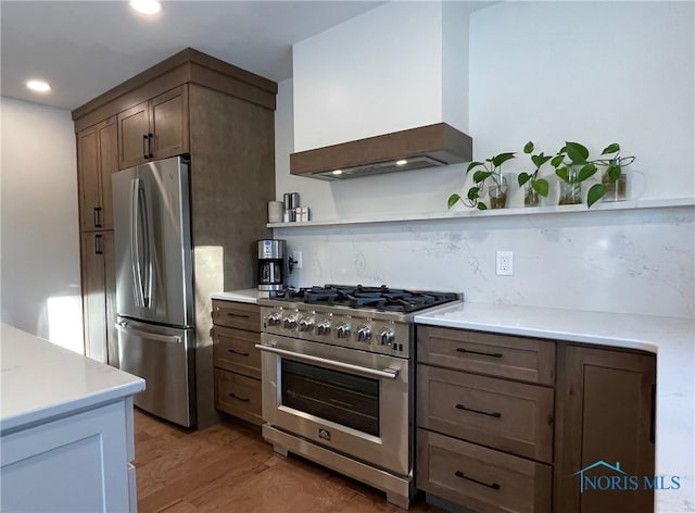 kitchen featuring decorative backsplash, dark brown cabinetry, stainless steel appliances, custom range hood, and light hardwood / wood-style flooring