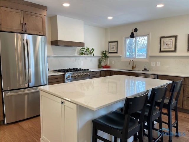 kitchen with a breakfast bar, sink, appliances with stainless steel finishes, a kitchen island, and light hardwood / wood-style floors