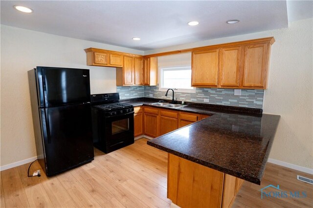 kitchen featuring a peninsula, a sink, decorative backsplash, black appliances, and dark countertops