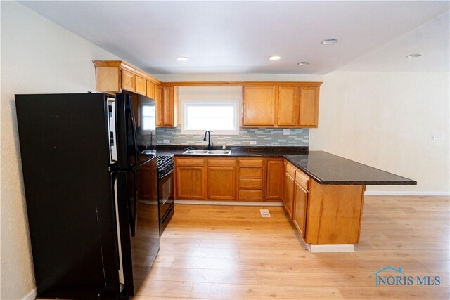 kitchen featuring a peninsula, a sink, light wood-style floors, backsplash, and black appliances