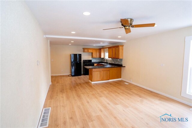 kitchen with a peninsula, a sink, visible vents, freestanding refrigerator, and dark countertops