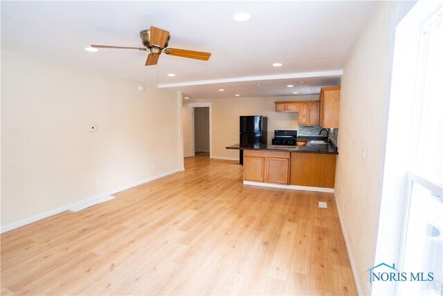 kitchen with dark countertops, freestanding refrigerator, open floor plan, a sink, and range