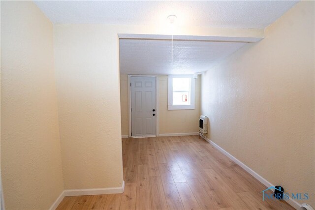 empty room featuring light wood finished floors, baseboards, a textured wall, heating unit, and a textured ceiling