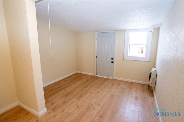 empty room featuring light wood-type flooring, a textured wall, a textured ceiling, and baseboards