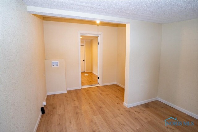 spare room featuring light wood-style flooring, baseboards, and a textured ceiling