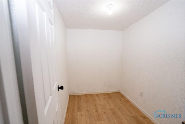 interior space featuring light wood finished floors, baseboards, and a textured ceiling