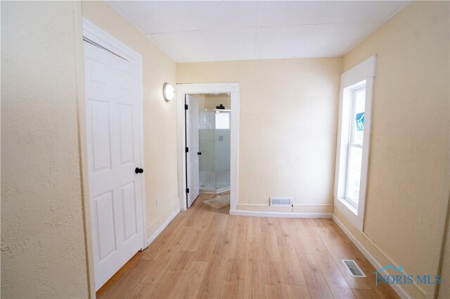 hall with light wood finished floors, baseboards, visible vents, and a textured wall